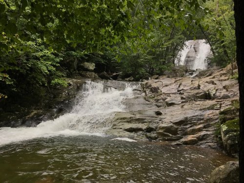 A serene waterfall cascades over rocky terrain, surrounded by lush green trees and a tranquil pool of water below.