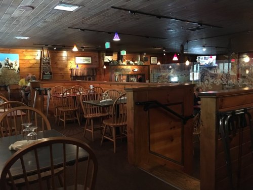 Cozy restaurant interior with wooden decor, empty tables, and colorful pendant lights.