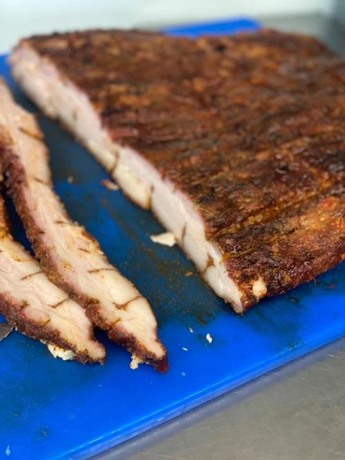 Sliced smoked meat on a blue cutting board, showcasing a crispy exterior and tender interior.