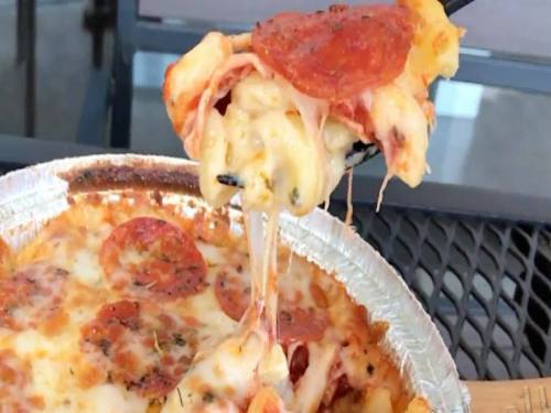 A fork lifting a cheesy, pepperoni-topped pasta dish from a foil container.