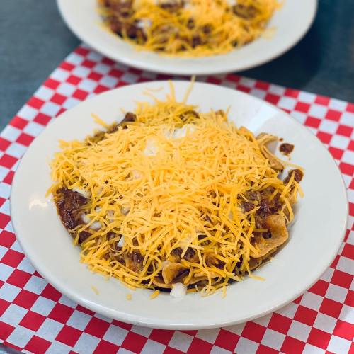 A plate of nachos topped with melted cheese, chili, and onions, served on a red and white checkered tablecloth.