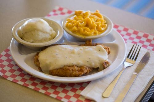 A plate of fried chicken smothered in gravy, served with mashed potatoes and macaroni and cheese on a checkered placemat.