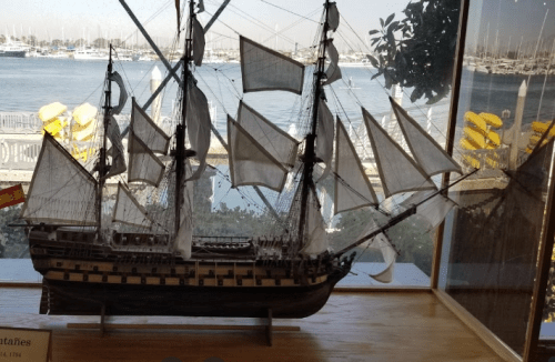 A detailed model of a tall ship with sails, displayed near a waterfront with boats in the background.