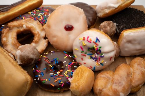A variety of donuts, including glazed, chocolate, and sprinkled, arranged on a wooden surface.