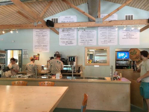 A bright café interior with staff at the counter, menus on the wall, and a casual dining area with wooden tables.