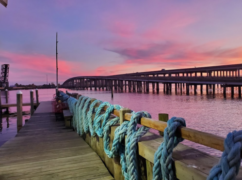 A colorful sunset over a bridge, with blue ropes coiled on a wooden dock by the water.