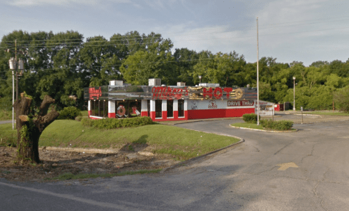 A colorful fast-food restaurant with a drive-thru, surrounded by greenery and a partially empty parking lot.