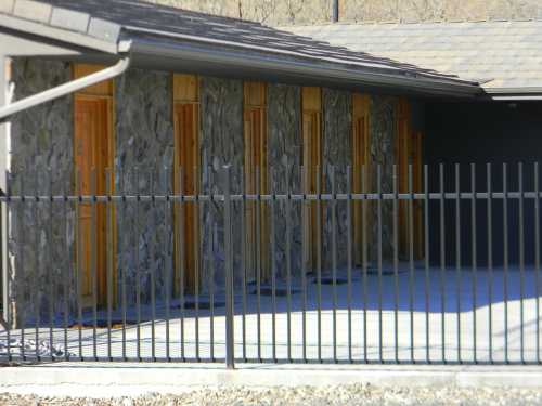 A stone building with wooden doors, partially enclosed by a black metal fence.