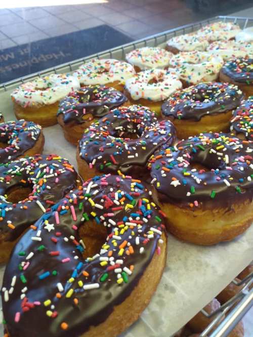 A tray of assorted donuts, some topped with chocolate icing and colorful sprinkles, others with white icing and sprinkles.