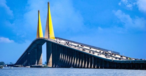 View of the Sunshine Skyway Bridge in Florida, featuring yellow cables and steady traffic, spanning over Tampa Bay, under a blue sky.