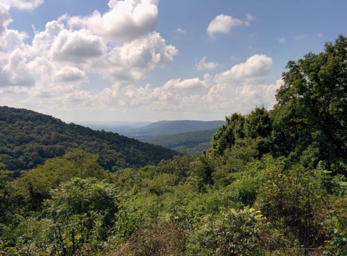 A scenic view of rolling green hills under a partly cloudy sky, with distant mountains in the background.