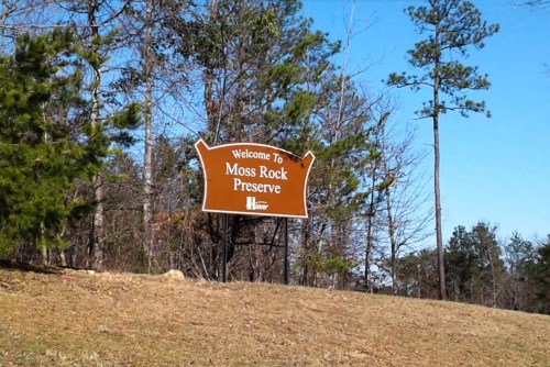 Sign welcoming visitors to Moss Rock Preserve, surrounded by trees and clear blue sky.