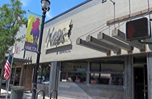 Exterior of a restaurant named "Max's Grill," featuring large windows and a street lamp, with an American flag nearby.