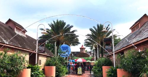 Entrance to a water park with palm trees, a sign reading "Cool Zone," and water fountains arching overhead.