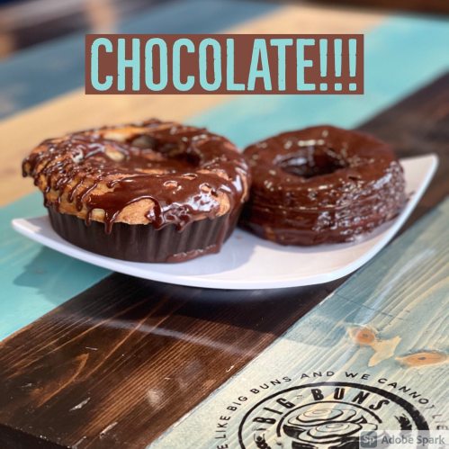 A plate with two chocolate desserts: a chocolate-covered pastry and a chocolate donut, on a colorful wooden table.