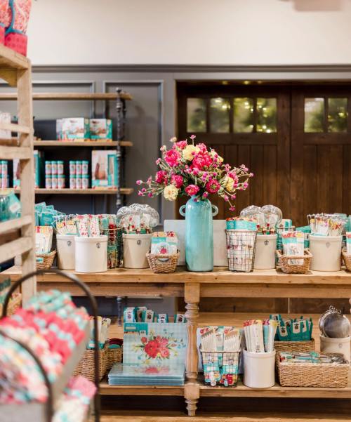 A cozy shop display featuring colorful stationery, baskets, and a vase of flowers on a wooden table.