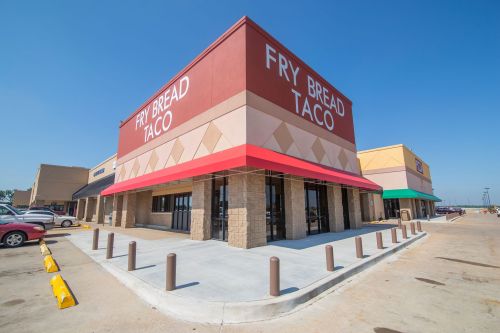 Exterior of a Fry Bread Taco restaurant with a red awning, clear blue sky, and parking lot in view.