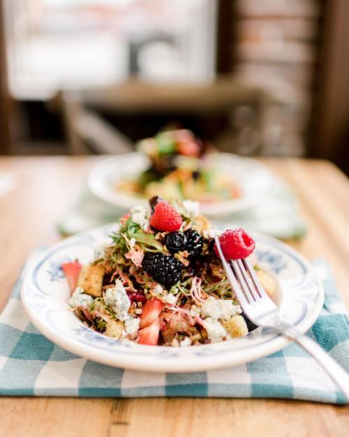 A colorful salad with mixed greens, berries, and cheese, served on a blue-patterned plate with a fork.