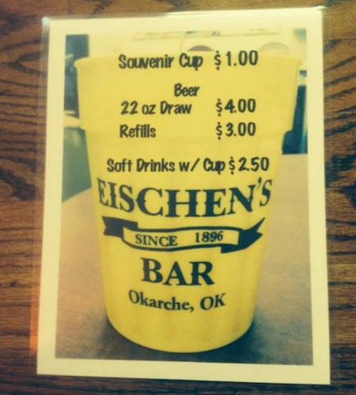 Menu sign featuring a yellow cup with prices for souvenirs, beer, refills, and soft drinks at Eischen's Bar, OK.