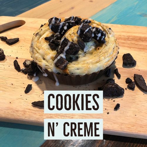 A baked cookies and cream dessert topped with crushed cookies, displayed on a wooden board.