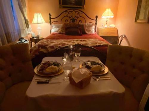 A cozy bedroom with a neatly made bed and a romantic dinner setup on a small table, featuring two plates and candles.