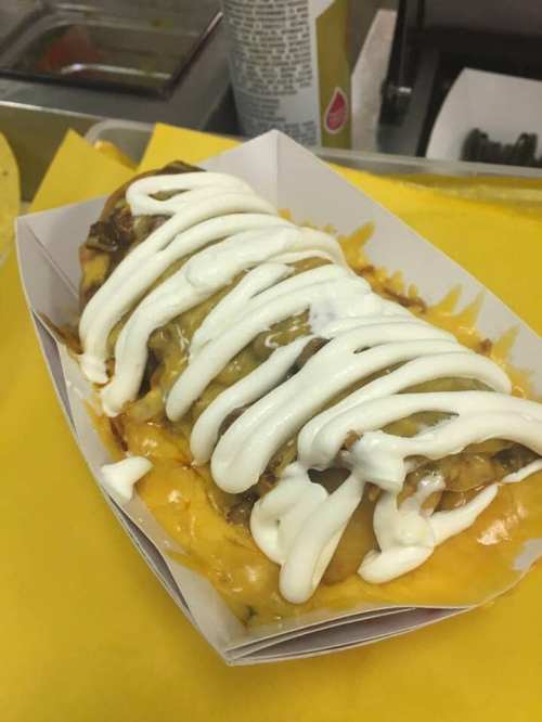 A loaded nacho dish topped with melted cheese and drizzled with sour cream, served in a paper tray.