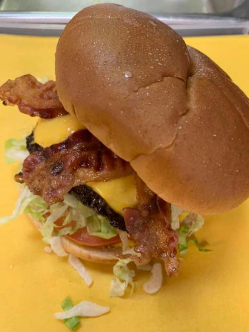 A delicious burger with melted cheese, crispy bacon, lettuce, and tomato, served on a soft bun.