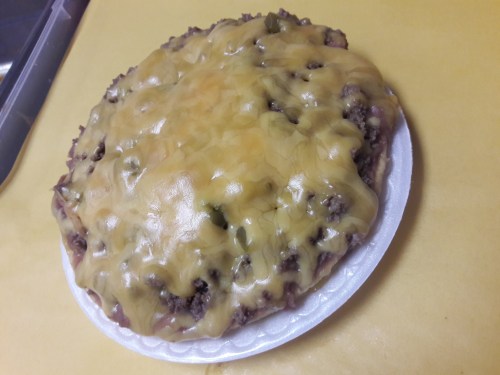 A round dish of cheesy beef casserole topped with melted cheese and green peppers on a white plate.
