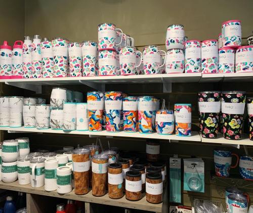 A display of colorful mugs and tumblers on shelves, featuring various patterns and designs.