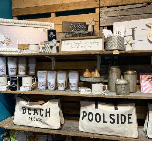 A display of home decor and kitchen items, including mugs, bags, and decorative signs on wooden shelves.