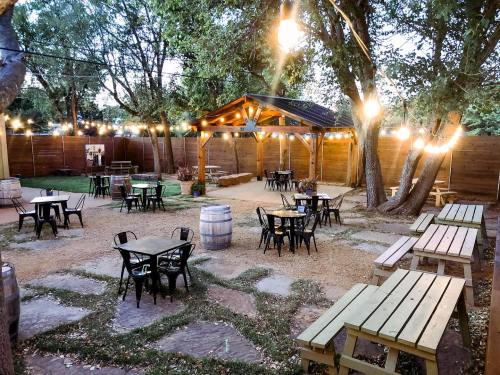 Outdoor seating area with wooden tables, string lights, and a gazebo surrounded by trees and a rustic fence.
