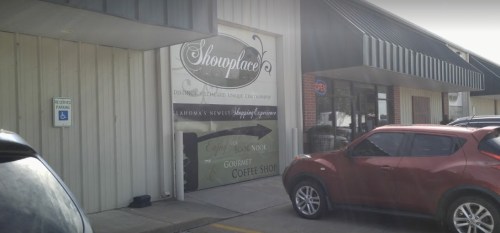 Sign for "Shopplace" with a coffee shop and book nook, next to parked cars outside a building.
