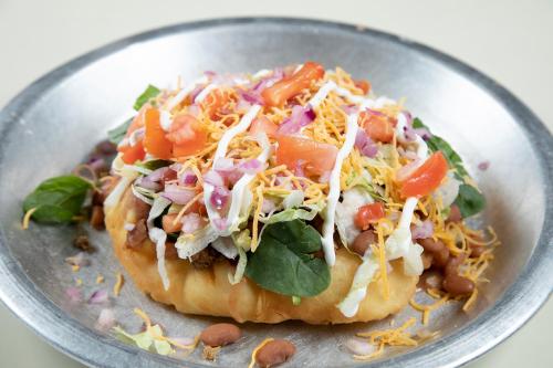 A colorful taco salad on a crispy shell, topped with lettuce, tomatoes, cheese, onions, and drizzled with sauce.