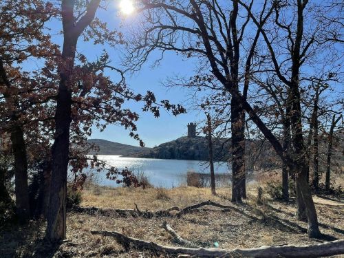 A serene landscape featuring a lake surrounded by trees, with a distant tower on a hill under a clear blue sky.