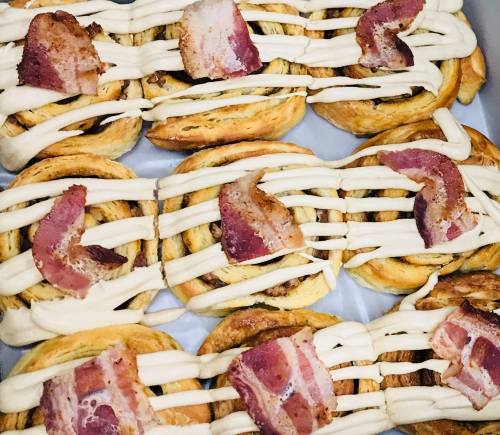 A tray of cinnamon rolls topped with cream cheese icing and pieces of crispy bacon.