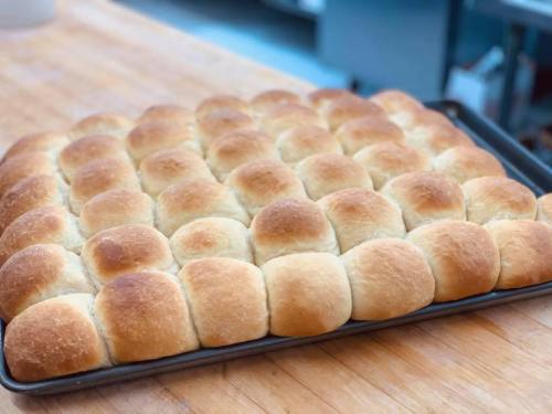 A tray of freshly baked golden-brown dinner rolls arranged in a neat grid on a wooden surface.