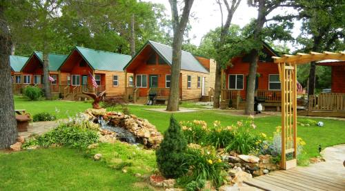 A scenic view of wooden cabins surrounded by greenery, flowers, and a small rock garden.