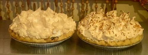 Two pies with fluffy meringue toppings, one with a light brown hue and the other with toasted coconut flakes.