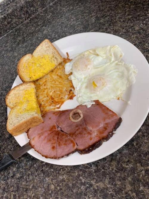 A plate with two fried eggs, ham slices, hash browns, and two pieces of toast with melted cheese.