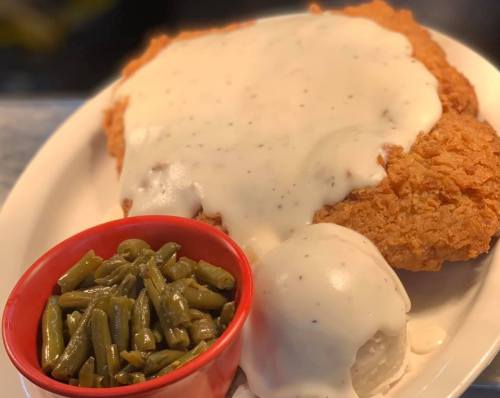 A plate of fried chicken topped with creamy gravy, served with green beans and a side of mashed potatoes.