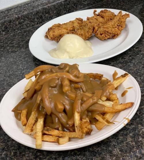 A plate of fries topped with gravy, alongside two pieces of fried chicken and a scoop of mashed potatoes.
