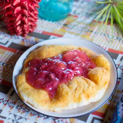 A golden fried pastry topped with a vibrant red fruit sauce, served on a decorative plate.