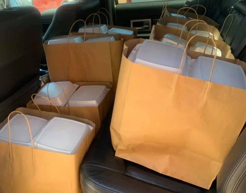 A car interior filled with large brown bags and white takeout containers.