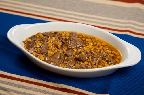 A white dish filled with beef and corn stew, served on a striped blue and beige tablecloth.