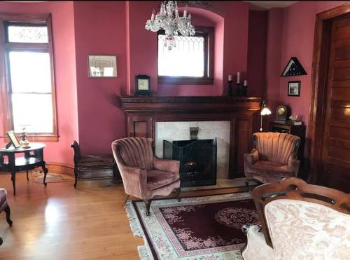 Cozy room with pink walls, vintage furniture, a fireplace, and a chandelier, creating a warm, inviting atmosphere.