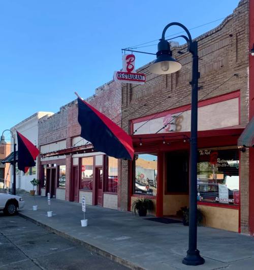 Exterior of a restaurant with red and black flags, a lamp post, and a clear blue sky in the background.