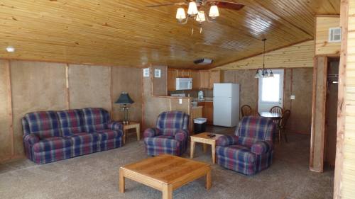 Cozy cabin interior with plaid sofas, wooden ceiling, dining area, and kitchen appliances. Warm and inviting atmosphere.