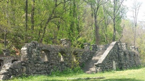 Stone ruins with arches and stairs, surrounded by lush green trees and foliage.
