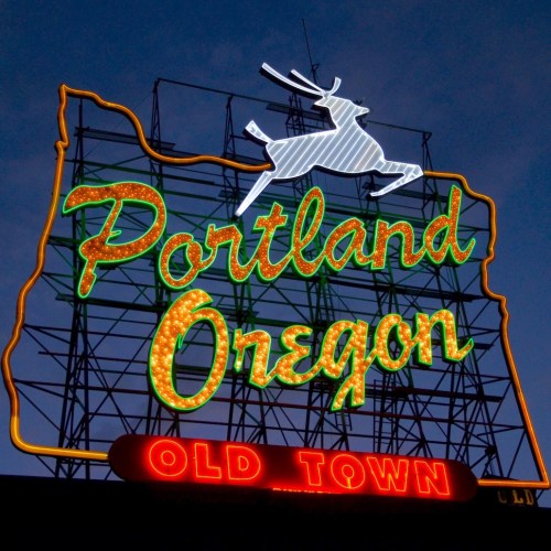 Neon sign of Portland, Oregon, featuring a leaping deer and the words "Portland Oregon Old Town" against a twilight sky.