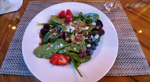 A fresh salad with spinach, berries, nuts, and feta cheese on a white plate, set on a textured placemat.
